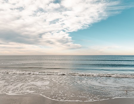 The image shows a serene beach with gentle waves lapping against the shore, under a sky filled with scattered clouds and a gradient of blue.