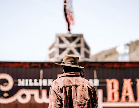 A person wearing a cowboy hat and jacket faces a large sign that reads 